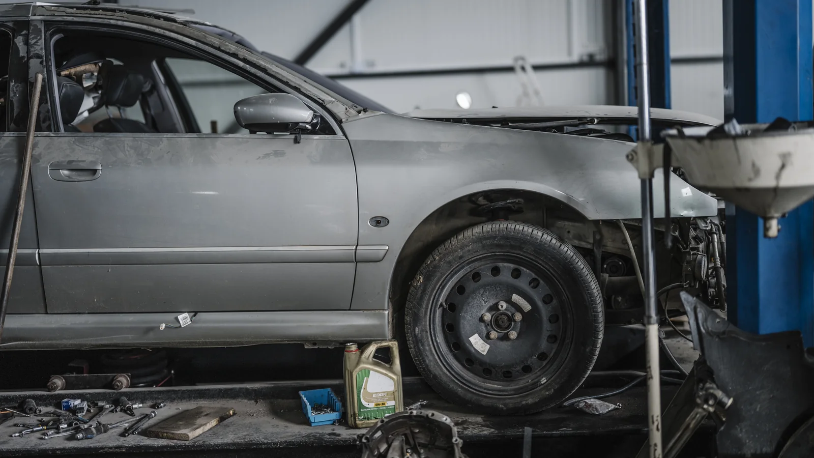 Voiture grise partiellement démontée dans un atelier automobile avec des outils au sol