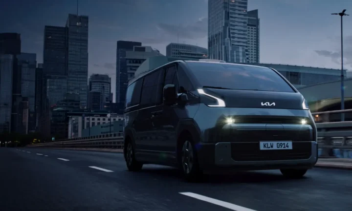 Kia PV7 électrique gris roulant sur une route urbaine devant des immeubles