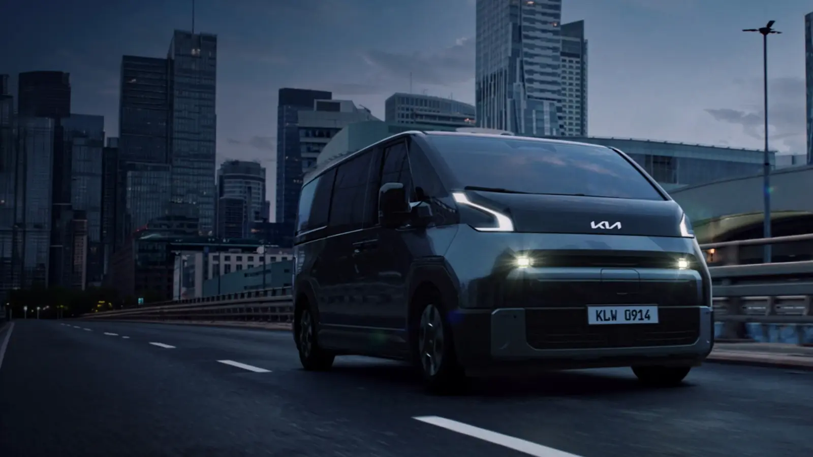 Kia PV7 électrique gris roulant sur une route urbaine devant des immeubles