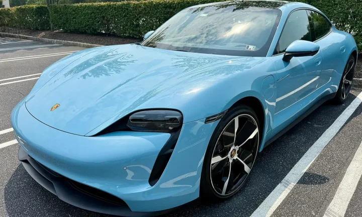 Porsche Taycan bleu clair photographié de trois quarts avant sur un parking