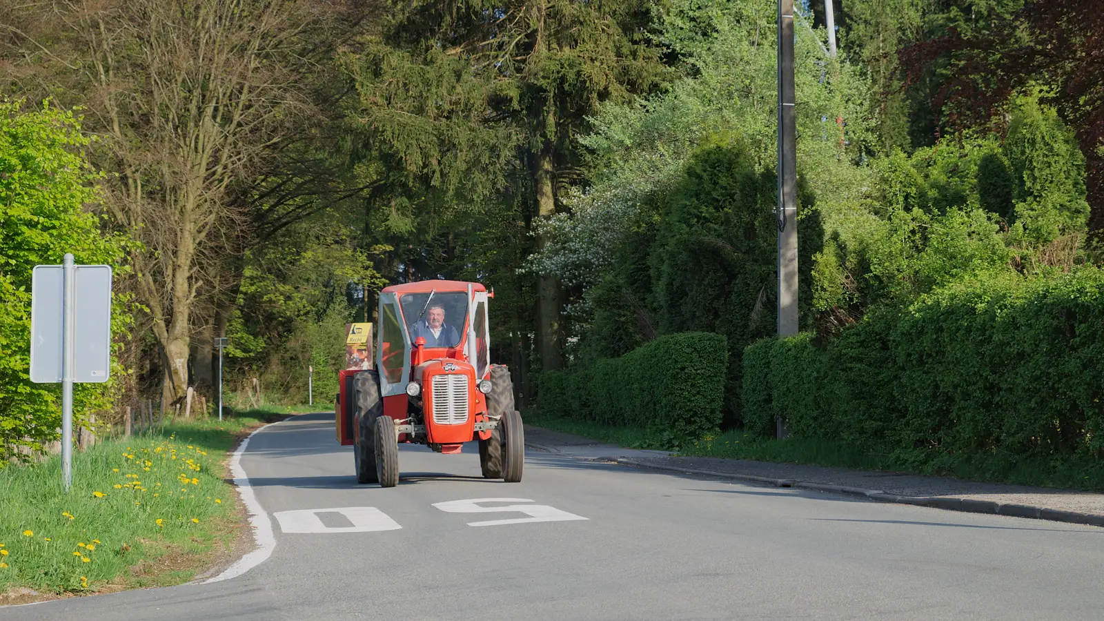 Tracteur rouge circulant sur une route bordée d’arbres à Saint-Vith