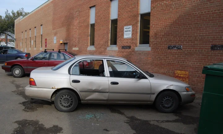 Voiture grise stationnée avec une vitre latérale brisée et des éclats au sol