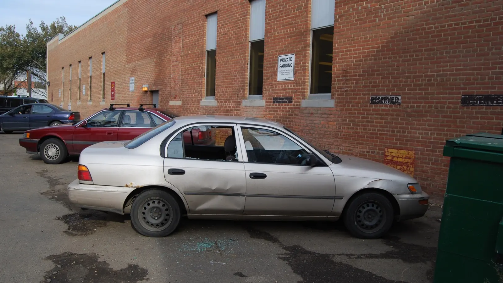 Voiture grise stationnée avec une vitre latérale brisée et des éclats au sol