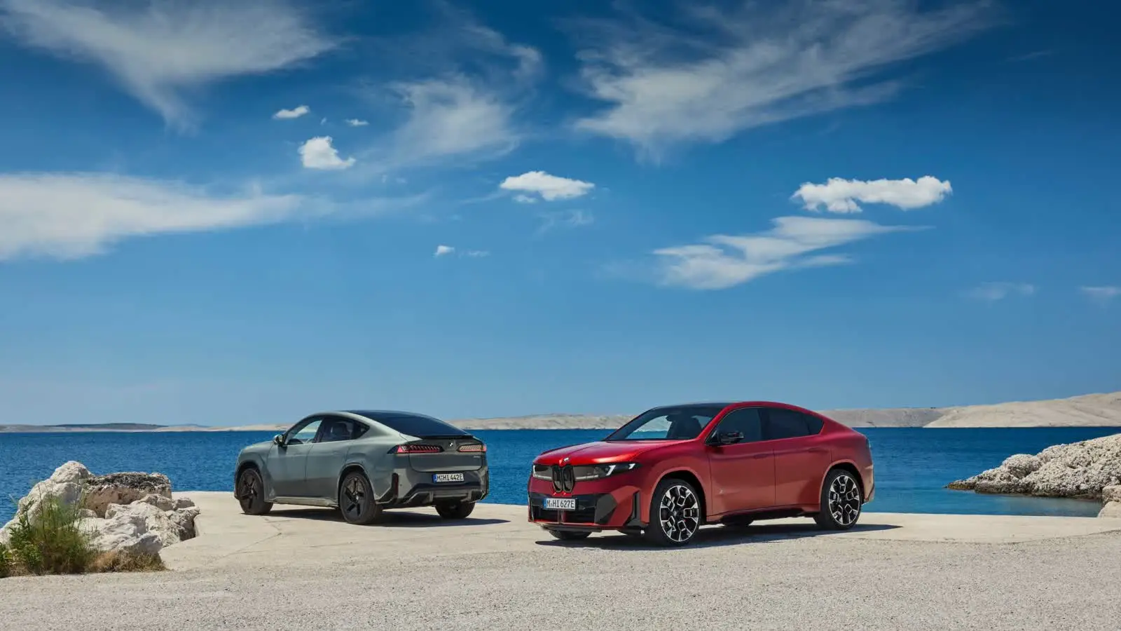 Deux BMW iX4 électriques rouge et grise au bord de la mer