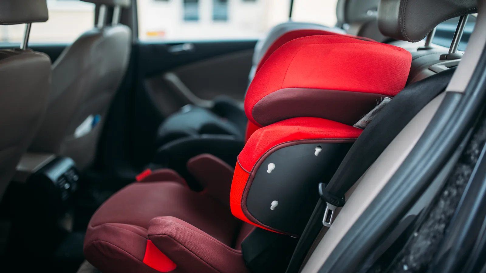 Siège auto rouge pour enfant installé et attaché sur la banquette arrière d’une voiture