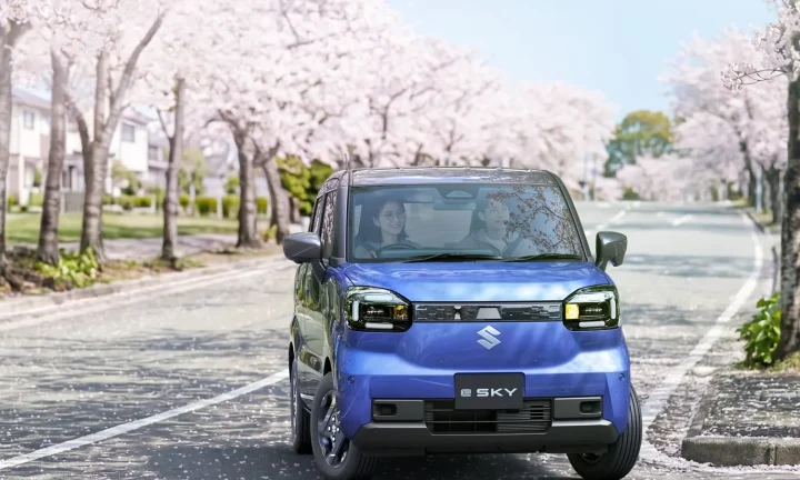 Suzuki e Sky bleue photographiée de face sur une route bordée de cerisiers au Japon